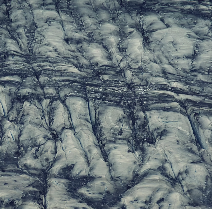 Close-up of a glacier's surface showing crevasses and ice formations with dark streaks and layers.