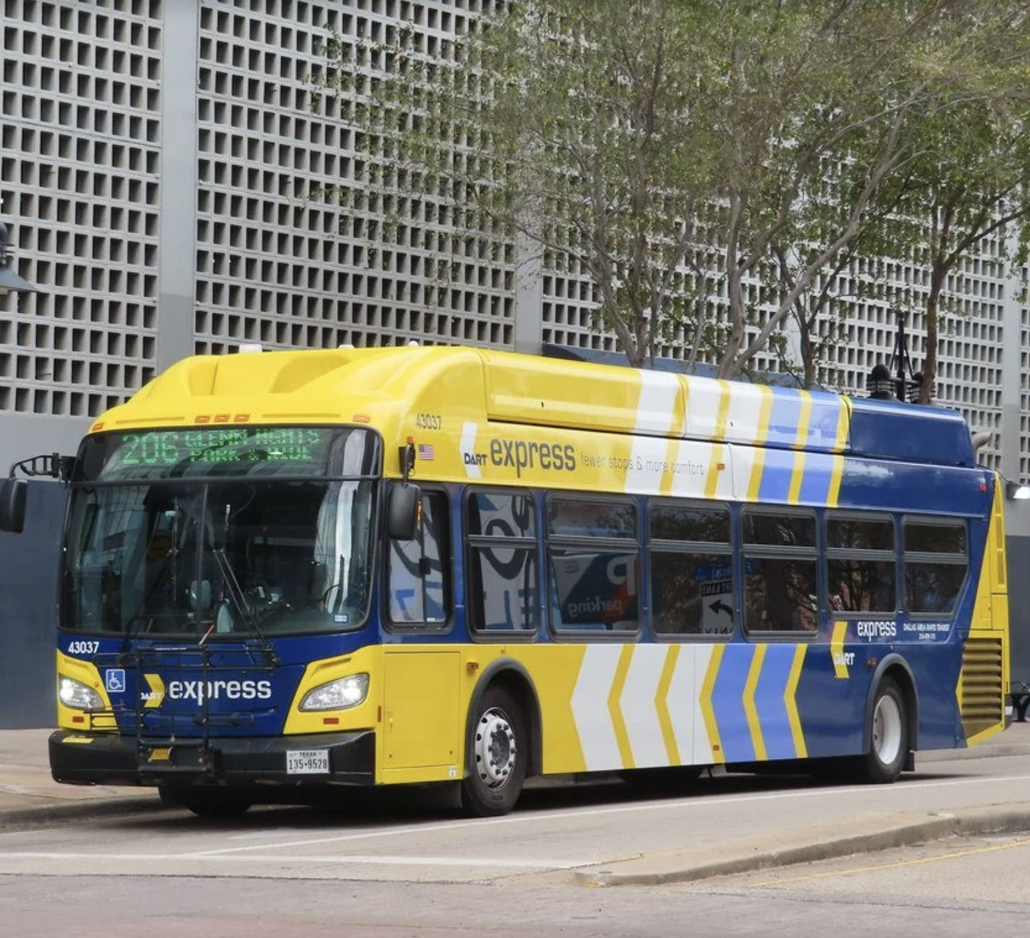 A yellow and blue MART Express bus parked at a bus stop with trees and a building in the background.