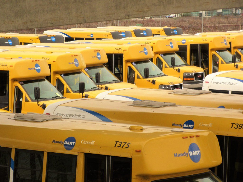 Multiple yellow transit buses parked in a lot, displaying 'Handy DART' and 'Canada' logos.