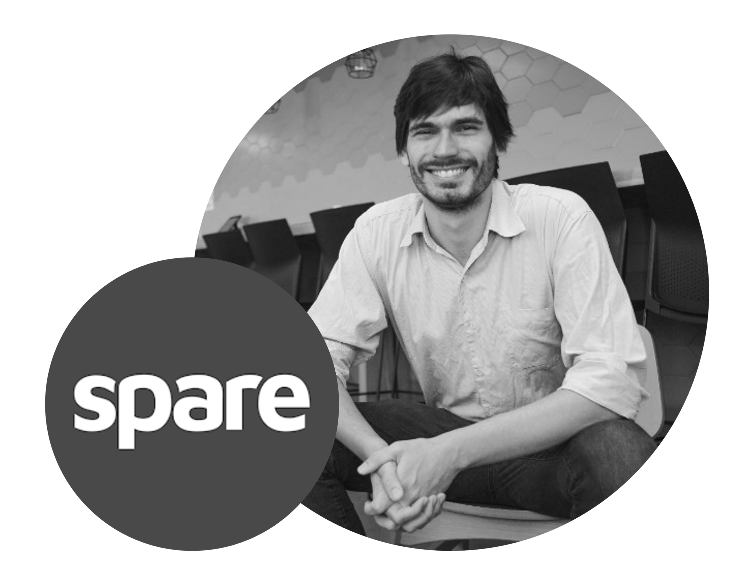 Black and white photo of a smiling man sitting at a table in a modern, casual office space. The man has dark hair and a beard, wearing a light-colored button-up shirt. There is a logo with the word "spare" in a dark circle overlapping the bottom left of the photo.
