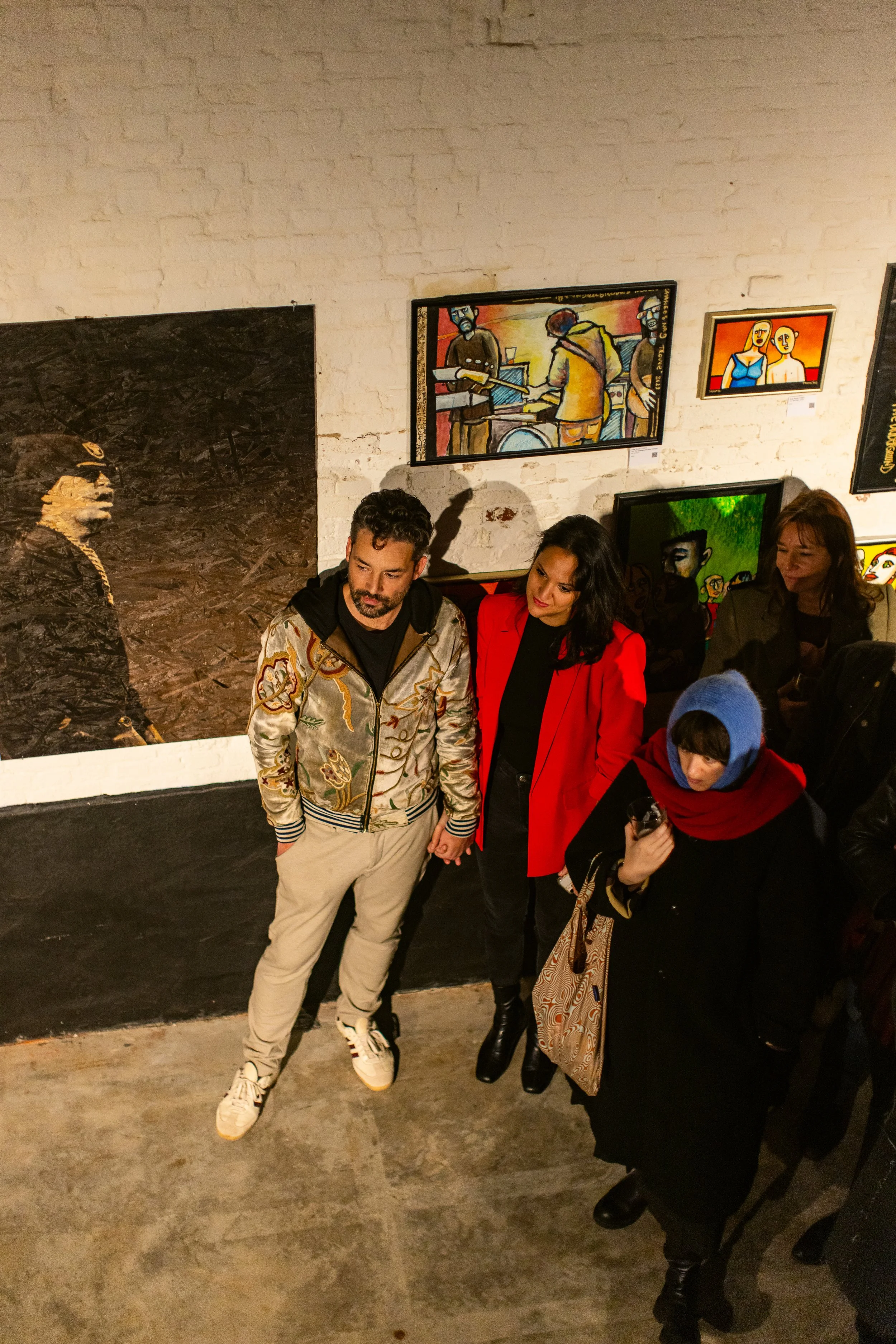 People viewing artwork in an art gallery with paintings on the brick wall.