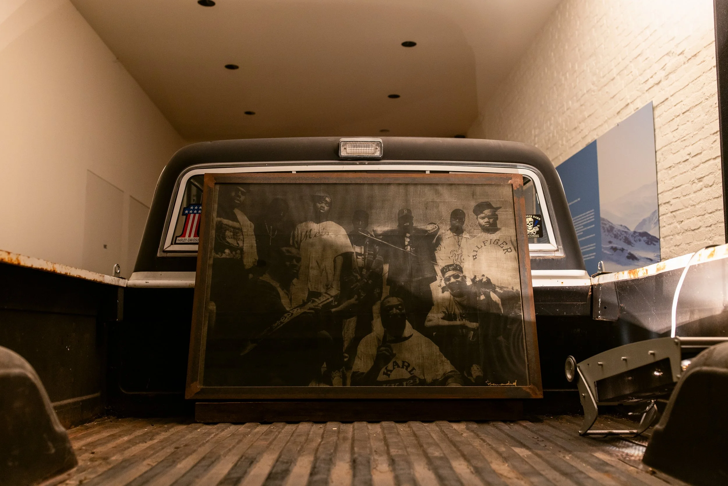 A black pickup truck with a vintage black-and-white photograph displayed on its rear window. The photograph shows a group of men, some holding musical instruments, in a historic, old photo style.