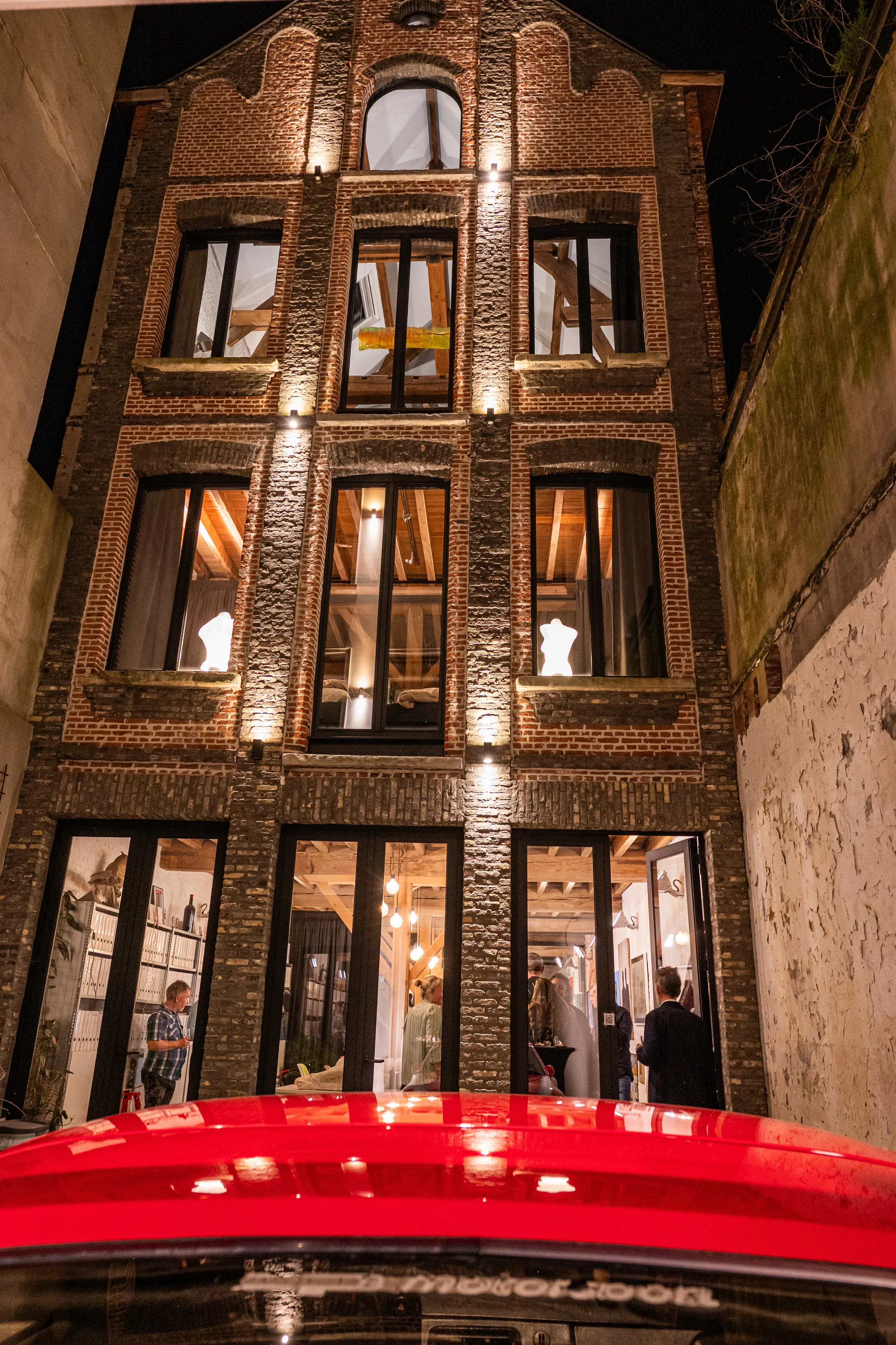 An old brick building with large windows at night, lit from within, revealing a group of people inside.