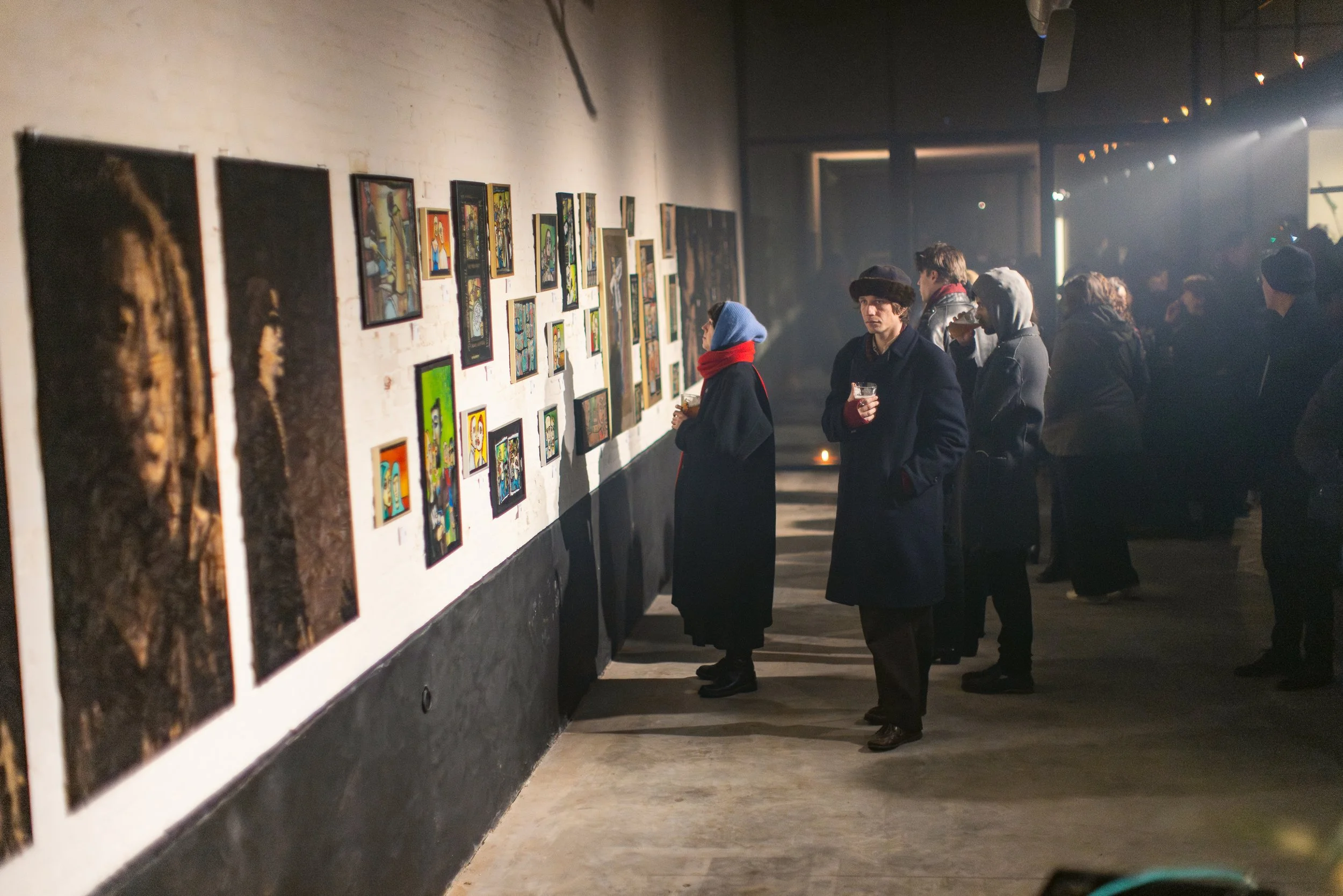 People viewing artwork in an art gallery with dim lighting and an assortment of framed art on the white wall.