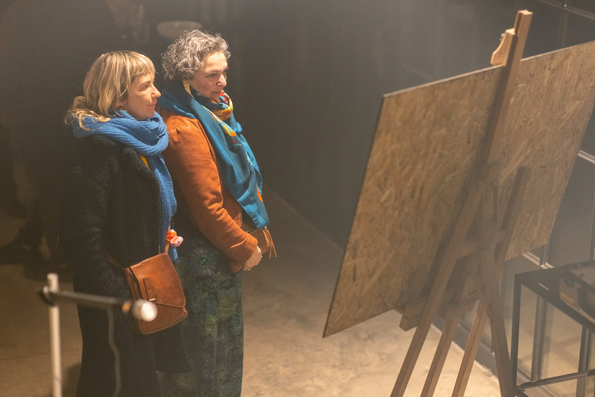 Two women looking at artwork displayed on easels in an art gallery.