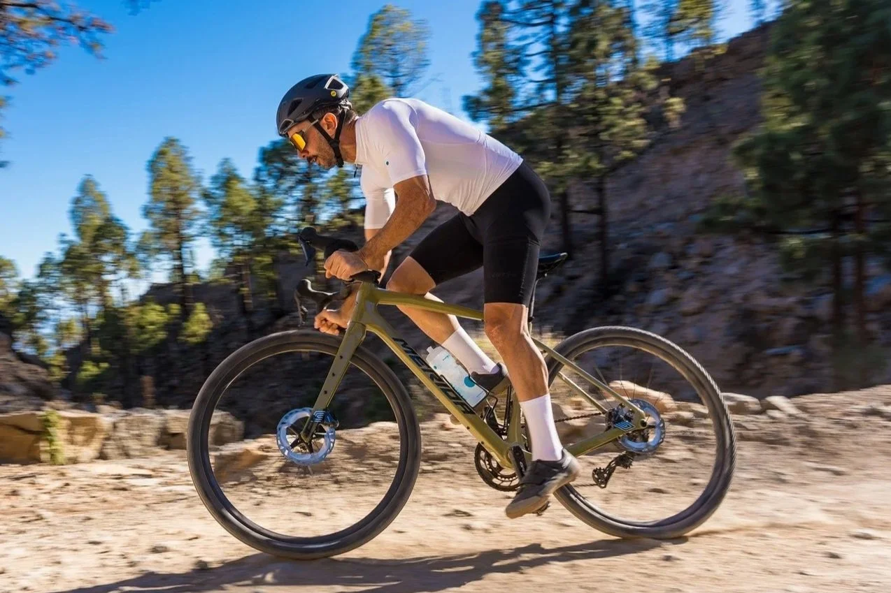 Uomo che fa mountain bike su un sentiero sterrato in una giornata soleggiata, indossa casco e abbigliamento sportivo.