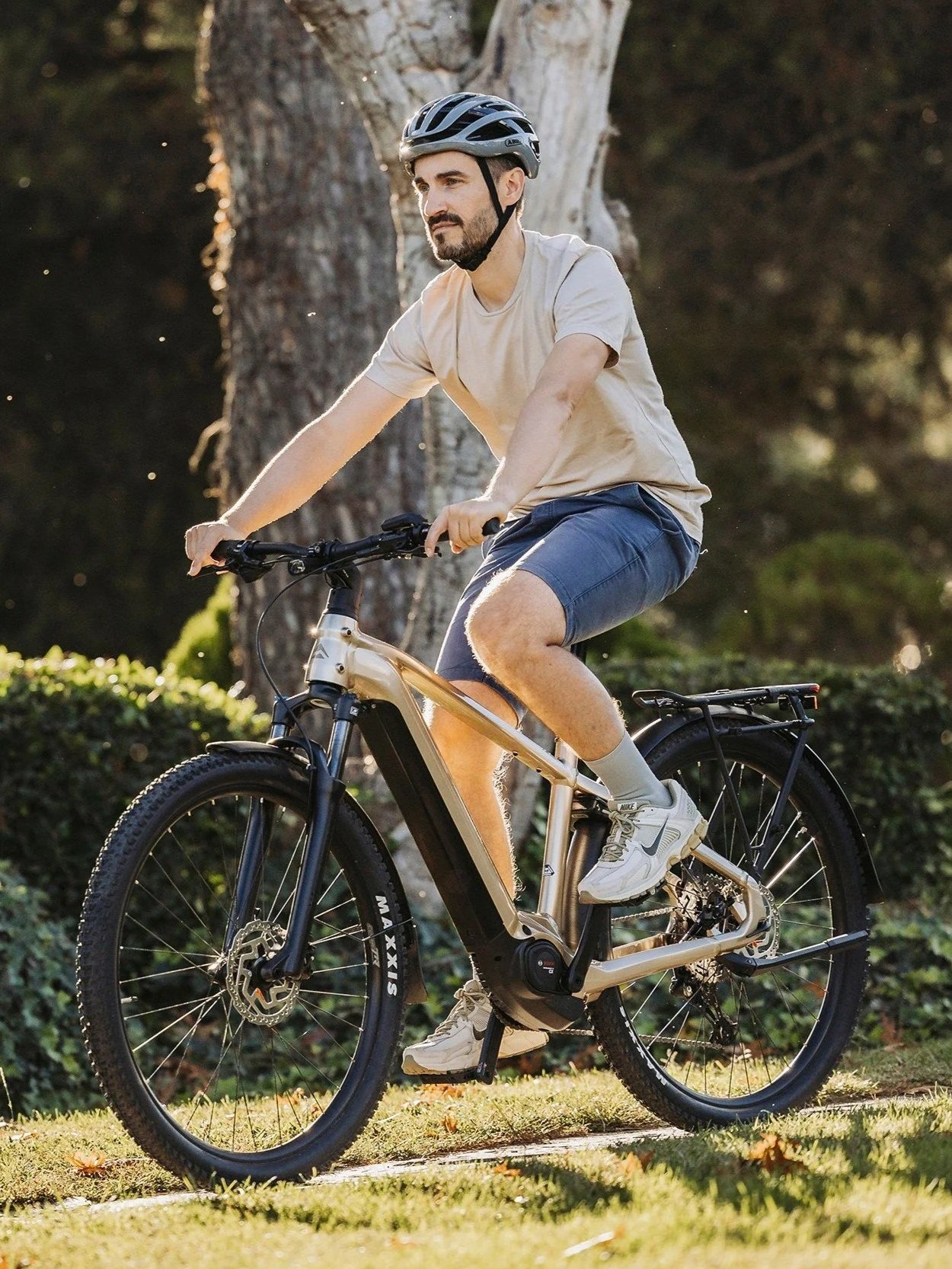 Uomo che pedala su una bicicletta elettrica in un'area verde con alberi, indossa un casco e abbigliamento casual.