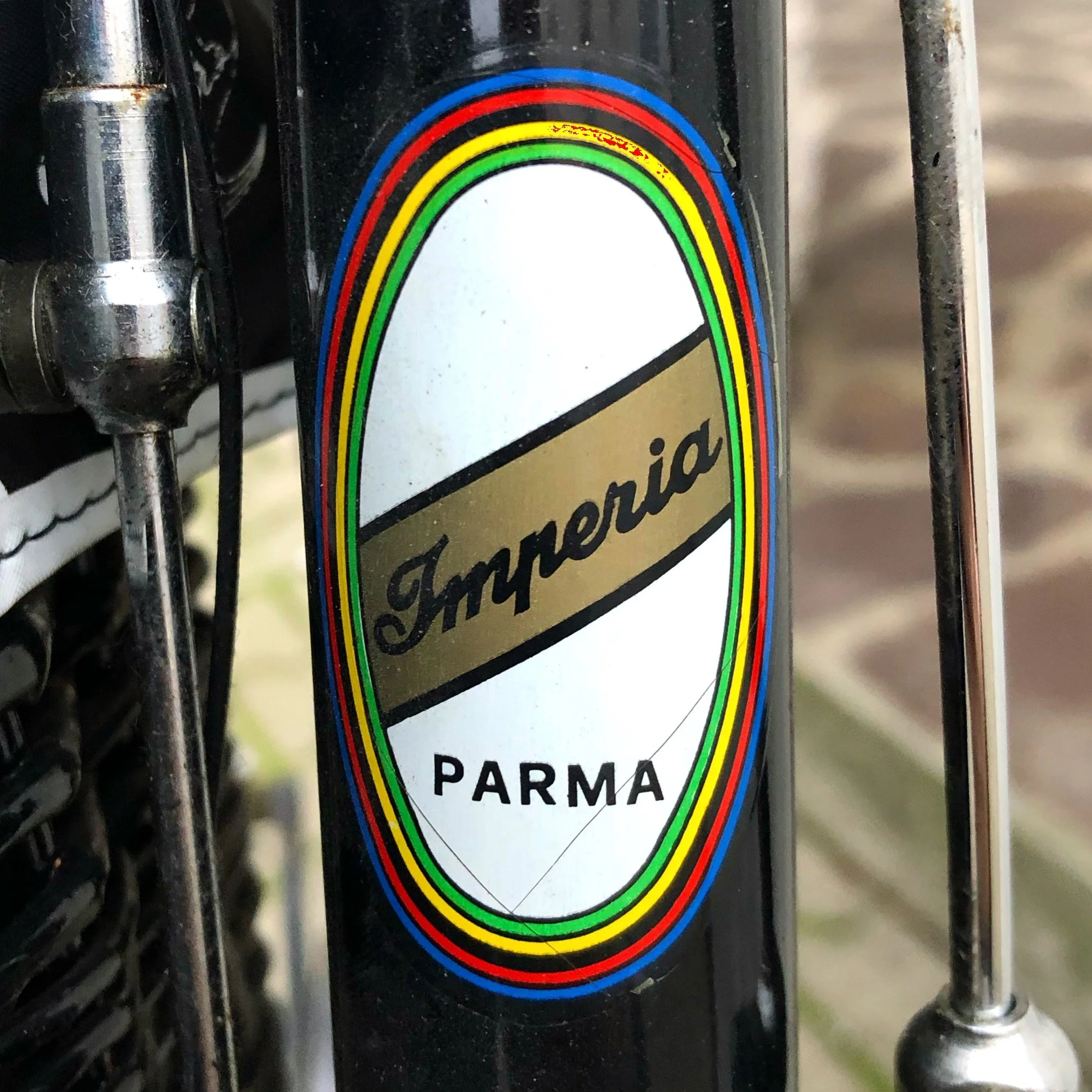 Dettaglio di una bicicletta con adesivo con il logo 'Imperia' e 'Parma' scritti, con decorazioni di strisce colorate.