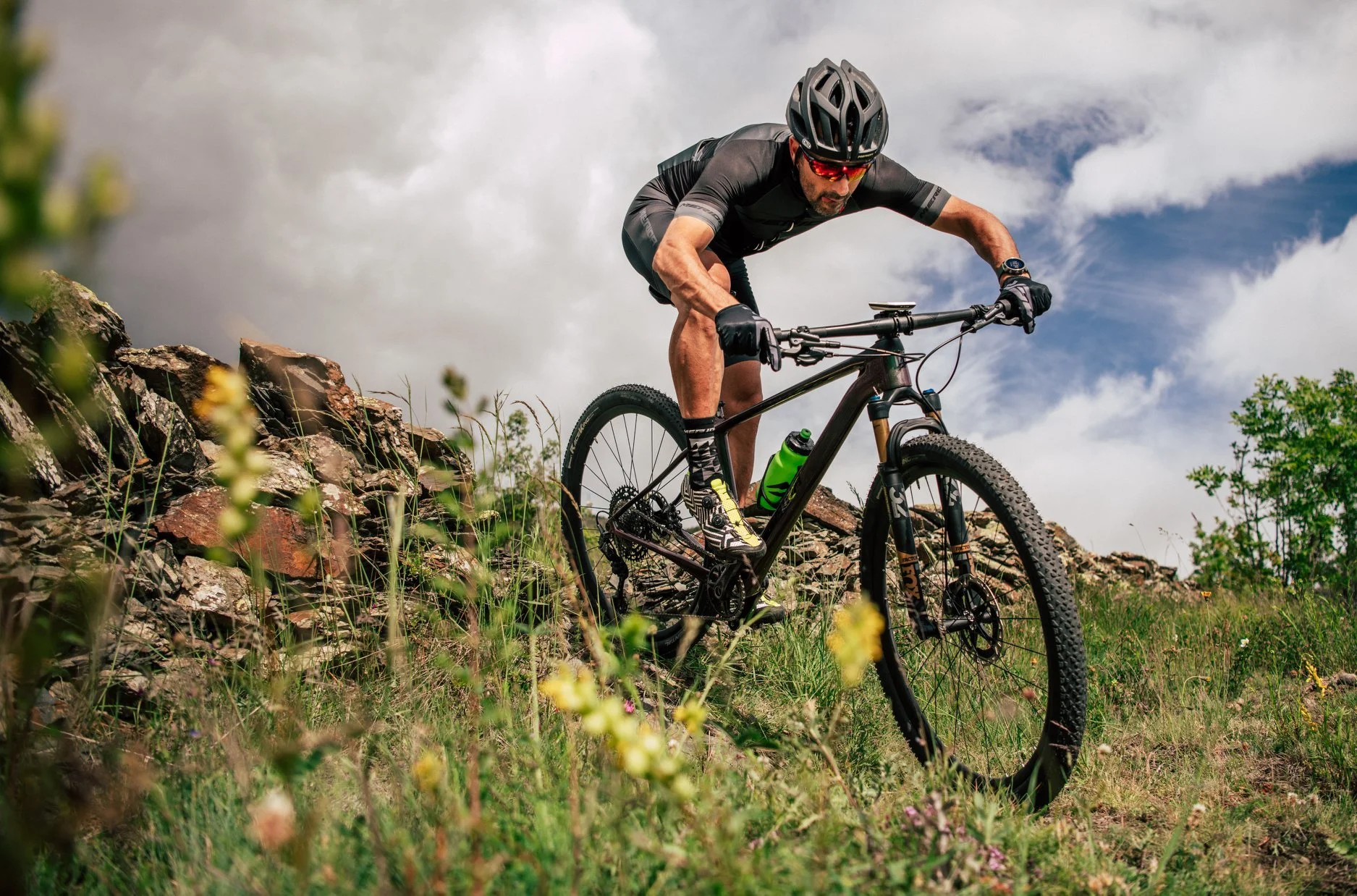 Uomo che pedala su una mountain bike su un terreno roccioso all'aperto con un cielo nuvoloso.