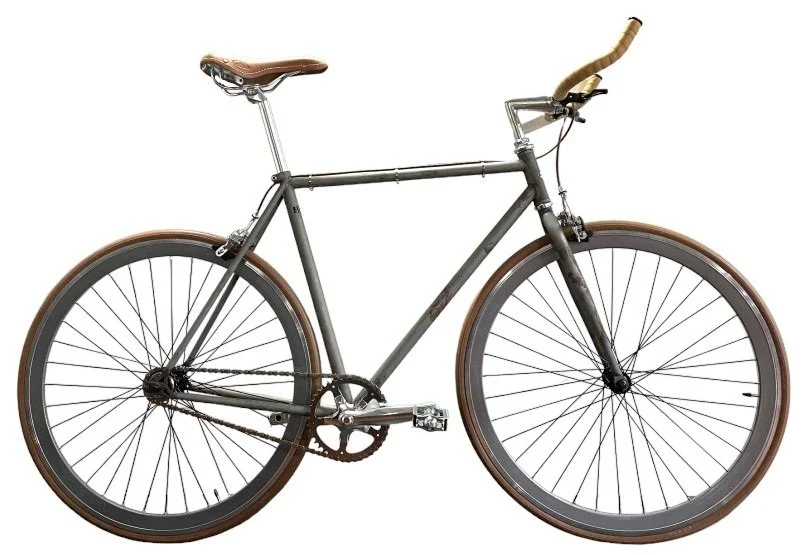 Bicicletta da corsa con telaio in metallo, manubrio curvato, sella in pelle e copertoni marroni.