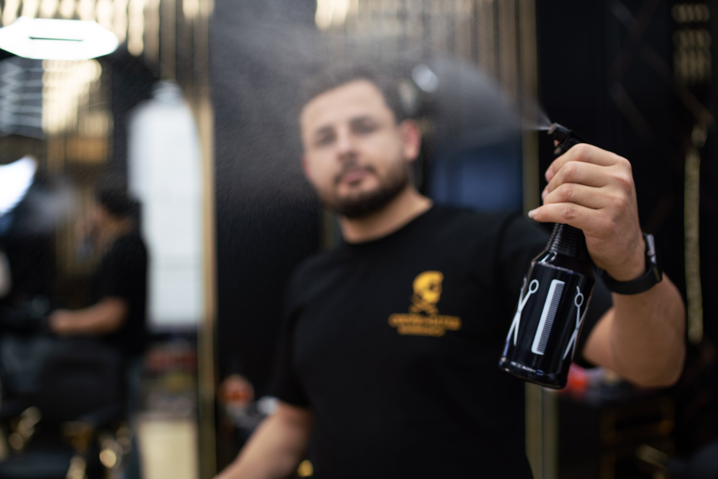 Schneider beim Haarschnitt in einem Friseursalon, während er ein Spray benutzt.