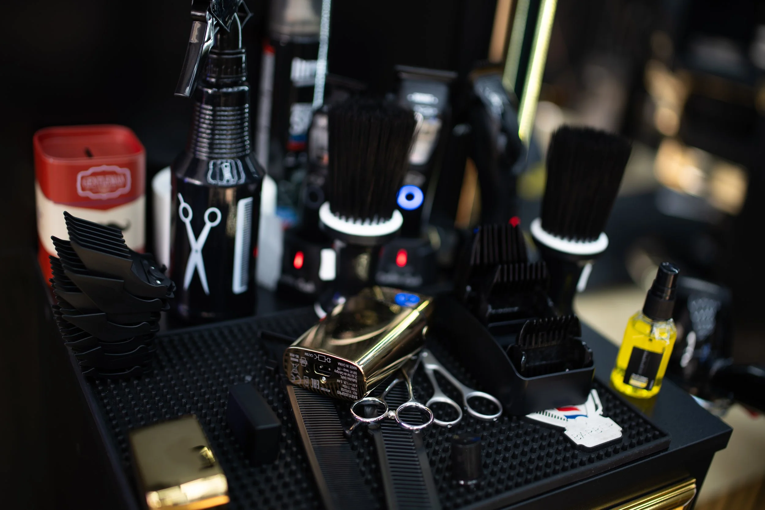 A black organizing tray on a table, filled with barber tools including scissors, a straight razor, combs, clippers, spray bottles, and other grooming products.