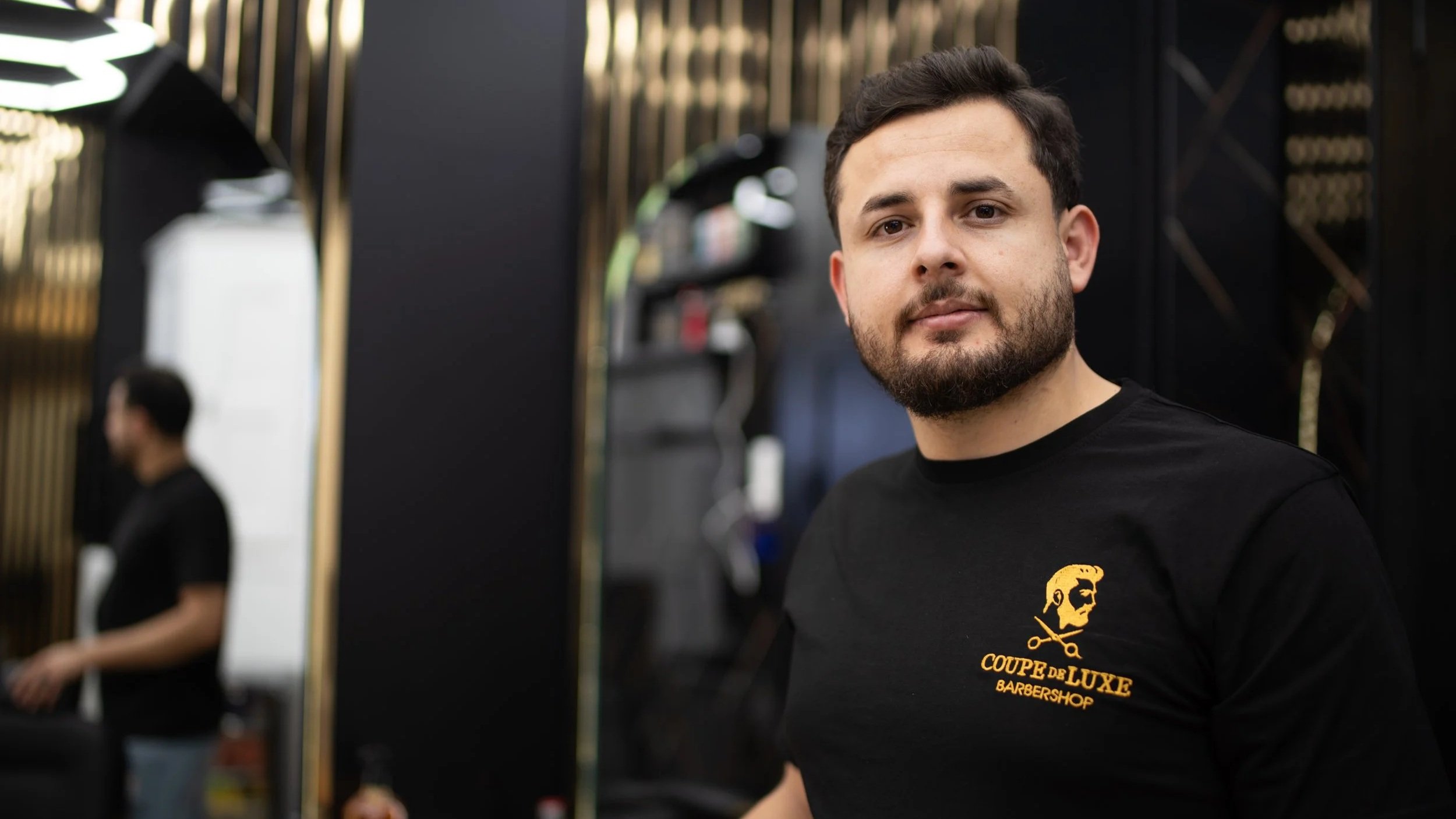 Mann mit Bart in dunklem T-Shirt mit Logo und Skull-Motiv im Friseursalon