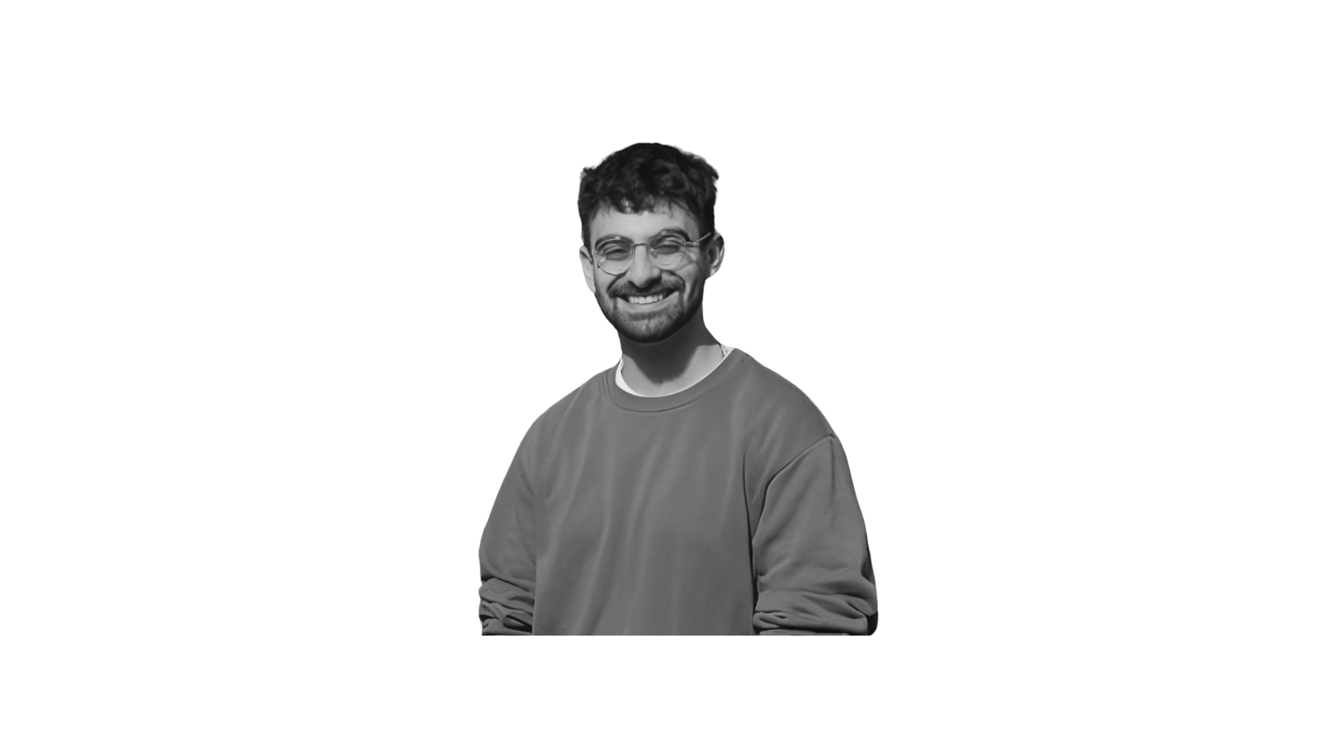 Black and white photo of a smiling man with glasses and a beard, wearing a sweatshirt, standing outdoors.