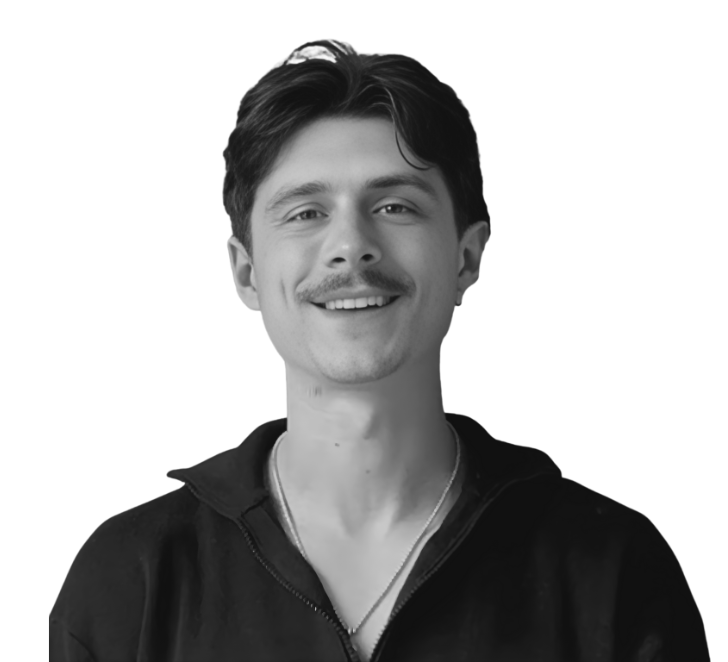 Black and white portrait of a young man smiling, wearing a zip-up jacket and a necklace.