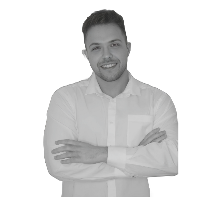 A young man with short hair, beard, and a smile, wearing a white dress shirt with arms crossed, standing against a plain background.