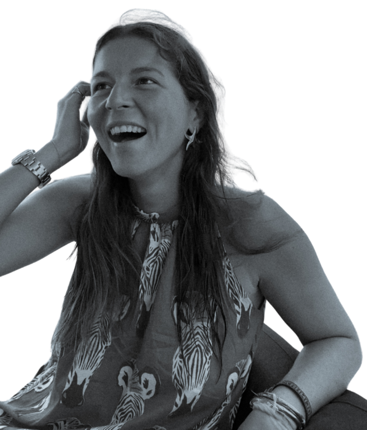 Une femme souriante avec des cheveux longs, portant un haut avec un motif de zèbres, des boucles d'oreilles, et plusieurs bracelets, en train de se toucher la tête.