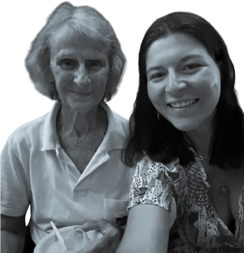 Deux femmes souriantes posent pour une photo, l'une plus âgée avec des cheveux gris, l'autre plus jeune avec des cheveux noirs, en intérieur avec un fond turquoise.