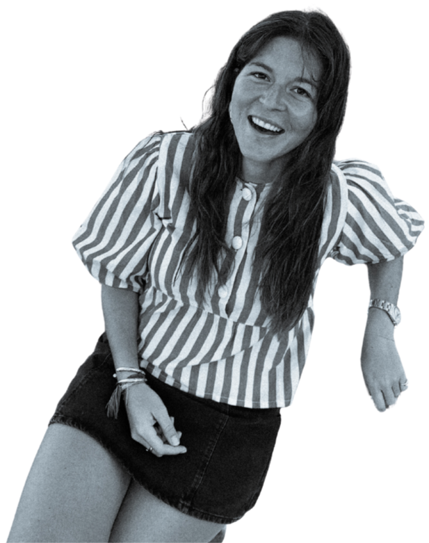 Une femme souriante avec des cheveux longs portant une chemise à rayures et une jupe, posant de manière détendue.