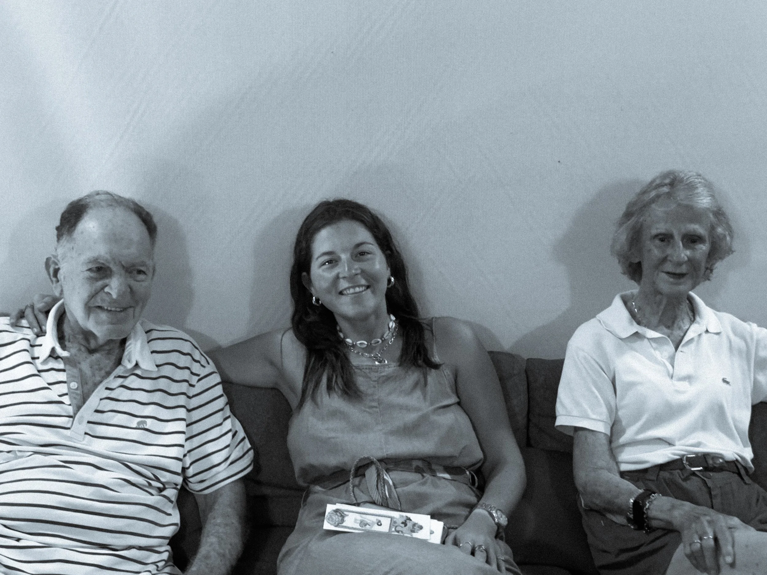 Trois personnes assises sur un canapé, deux hommes et une femme, sourire, intérieur.