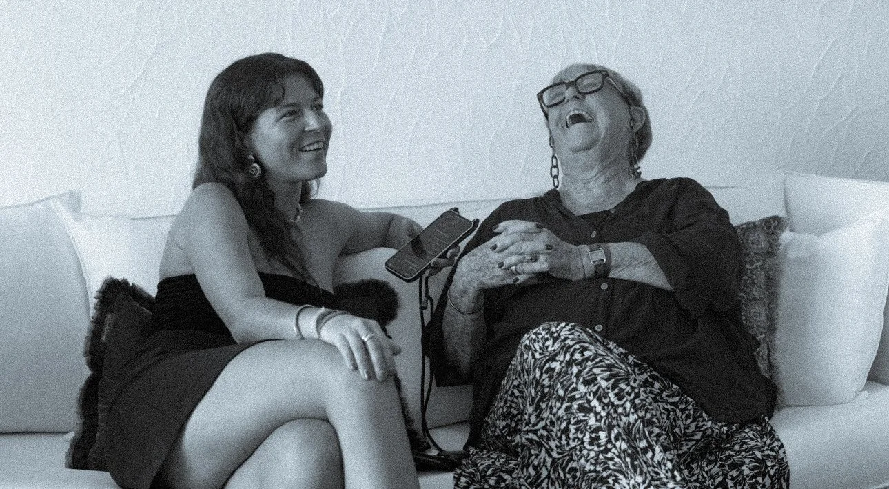 Deux femmes assises sur un canapé, une jeune femme souriante et une femme plus âgée riant.