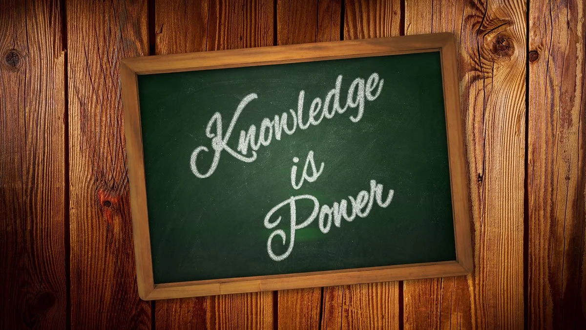 A green chalkboard with a wooden frame mounted on a wooden wall. The chalkboard has the phrase "Knowledge is Power" written in white chalk.