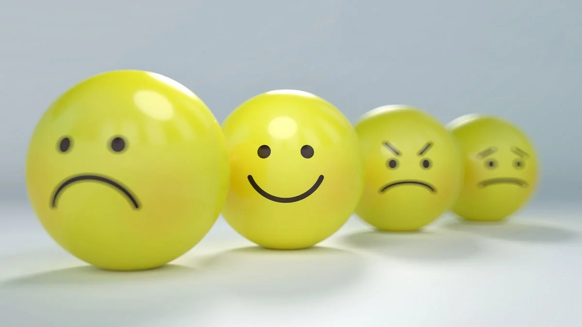 Four yellow balls with hand-drawn facial expressions reflecting different emotions, from sad to happy.