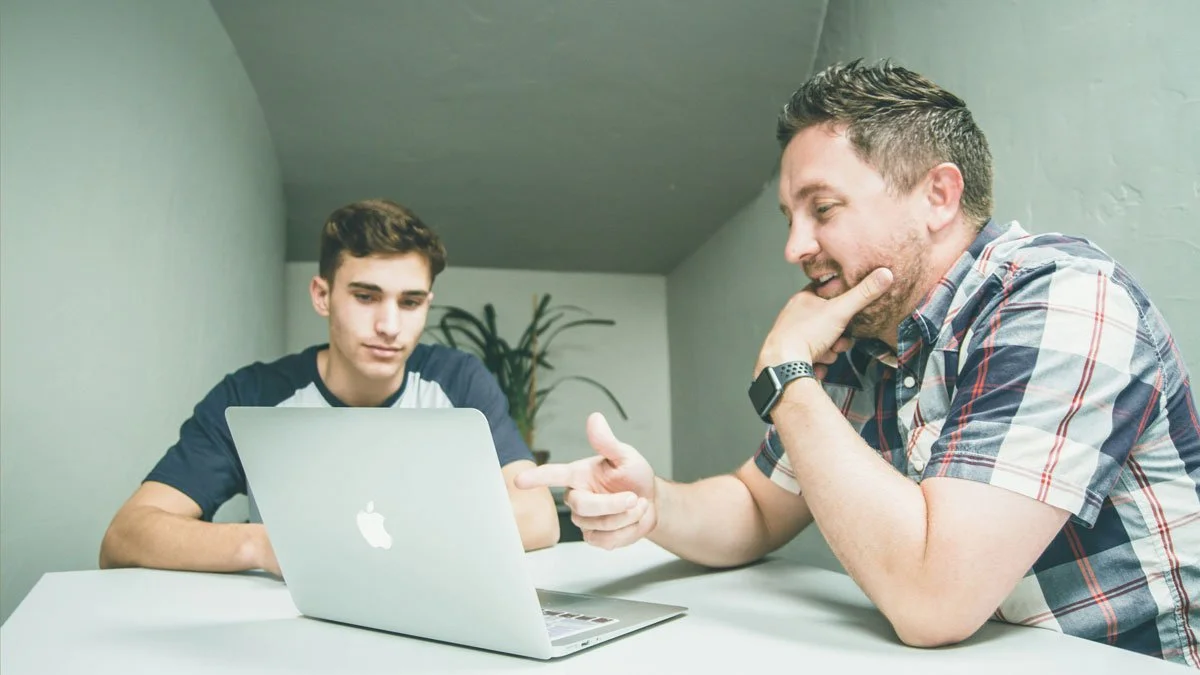Two men having a serious discussion in front of a laptop, in an office setting.