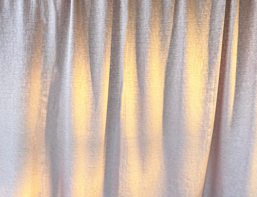 A beige curtain with soft lighting creating gentle shadows and folds.