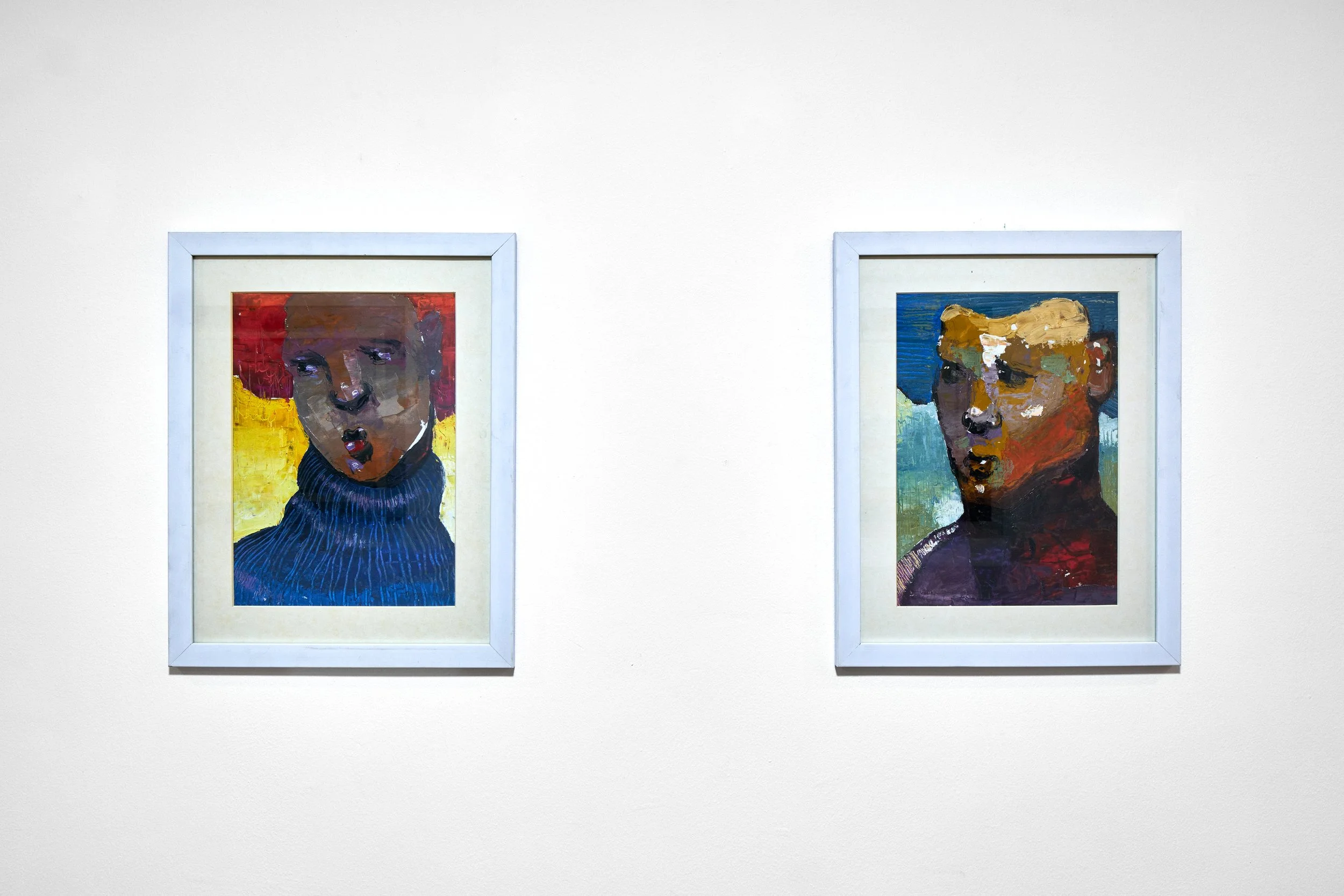 Two framed abstract portraits of women on a white wall, one with red hair and a blue turtleneck, the other with blonde hair and a multicolored background.