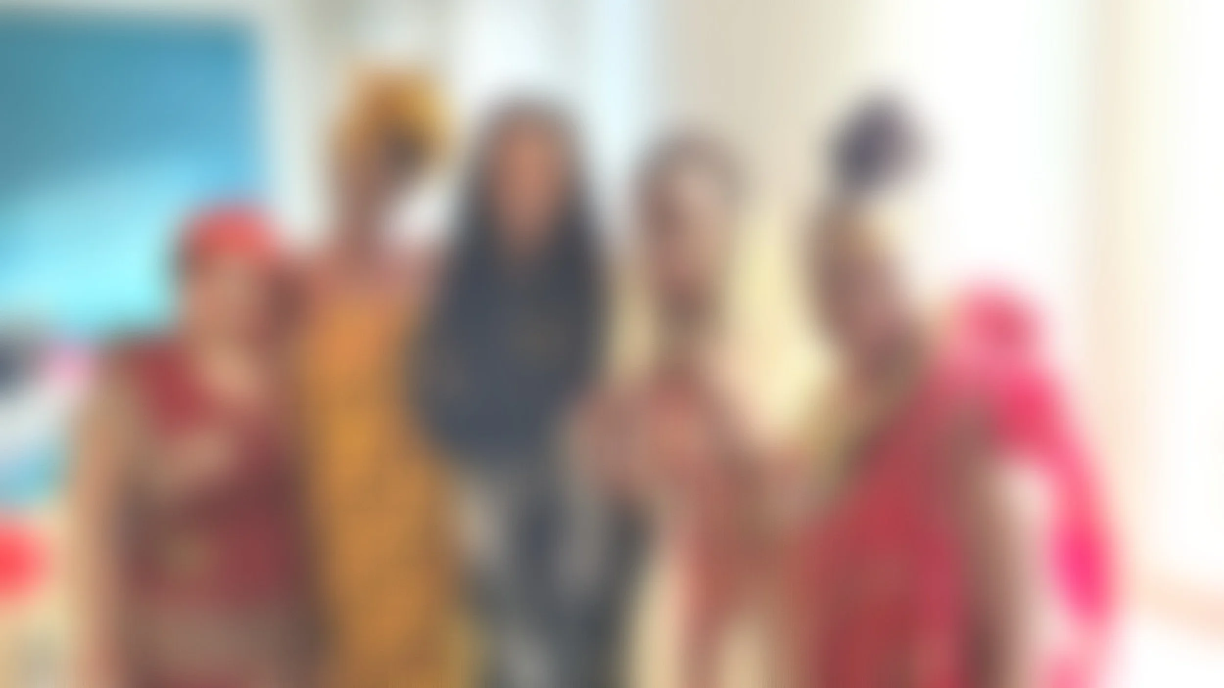 Blurred image of four women standing together indoors; background suggests a classroom or community space.