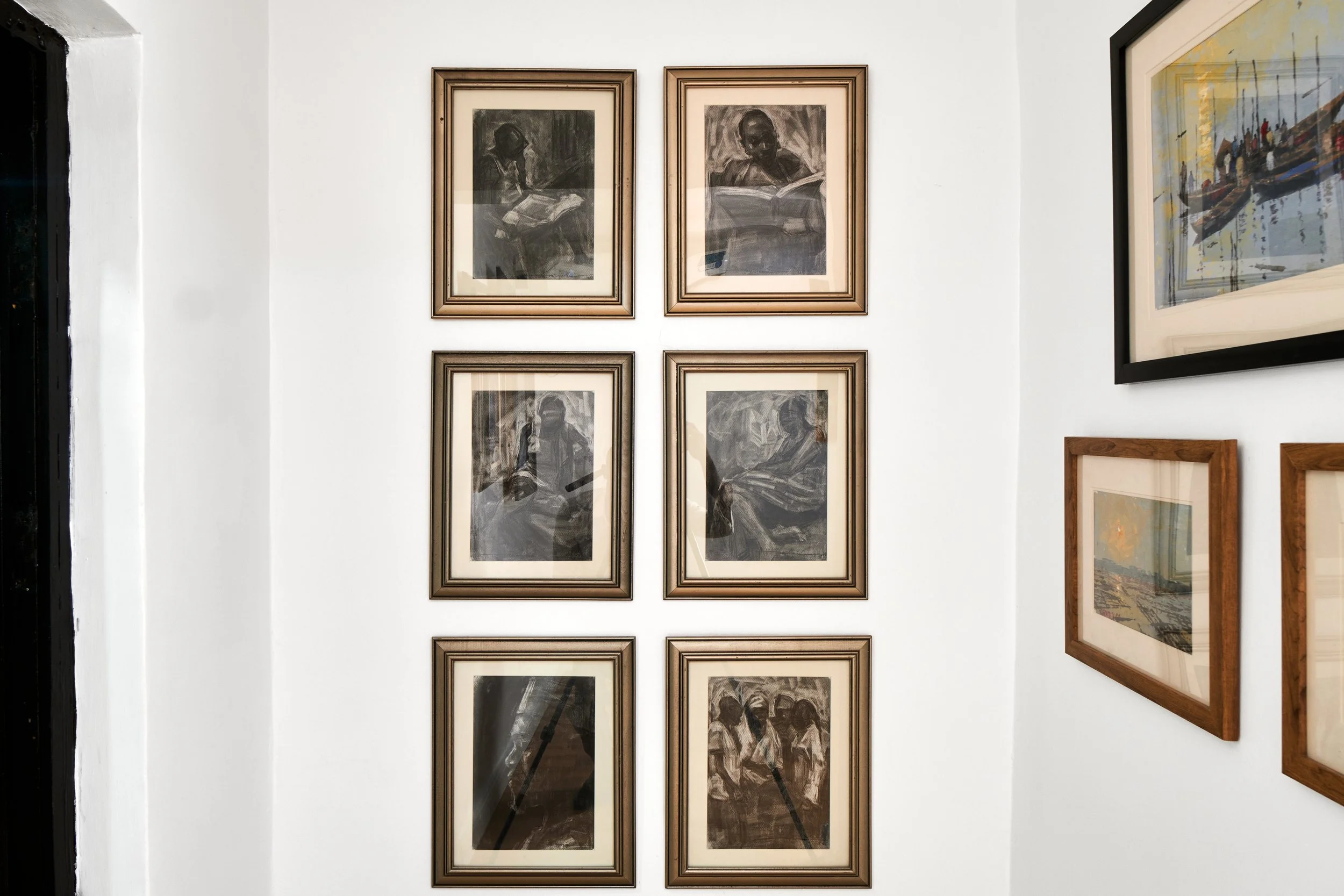 Gallery wall with six black-and-white framed photographs of children reading, arranged in three rows of two, on a white wall.