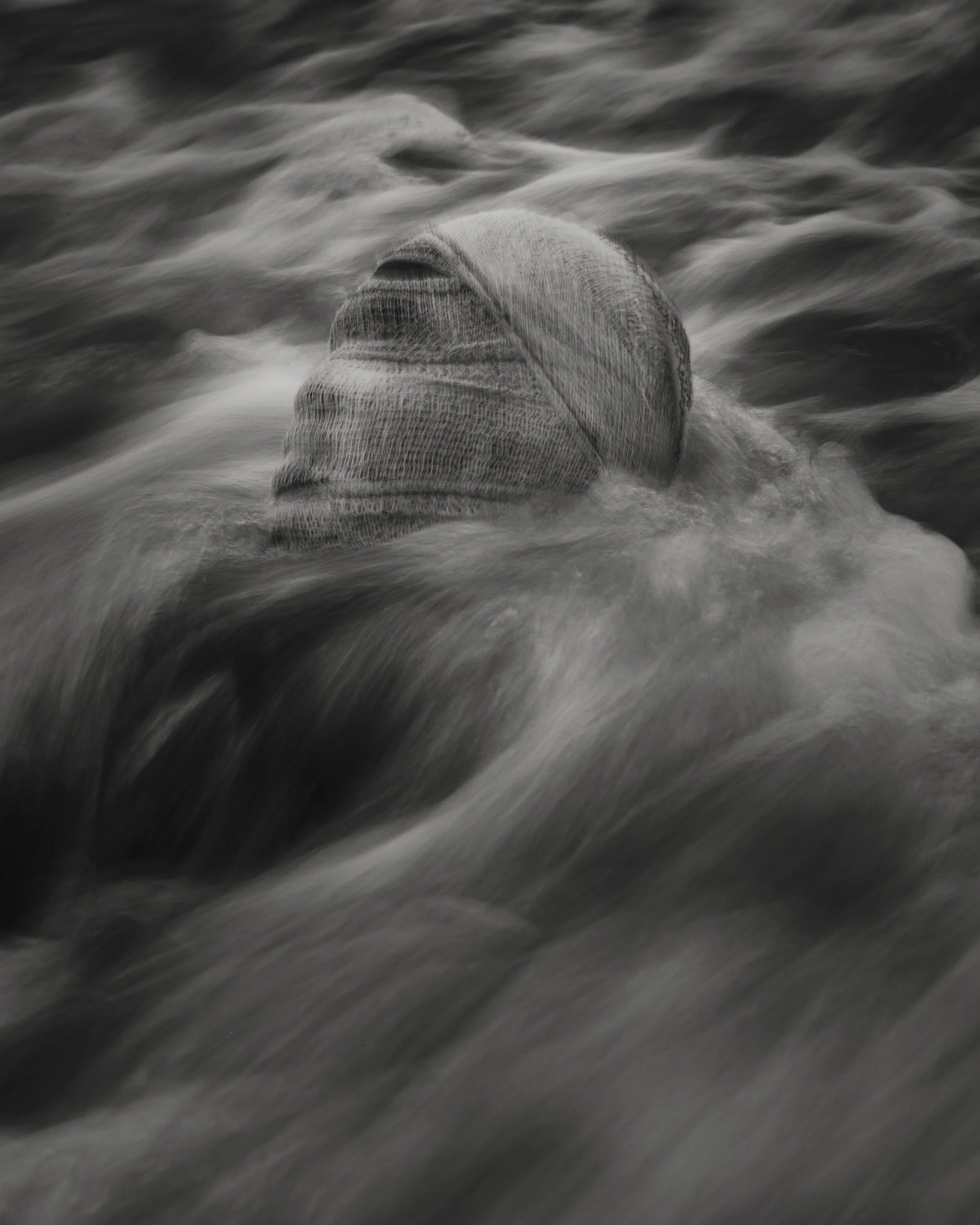 A person wrapped in bandages floating in water with waves rippling around.