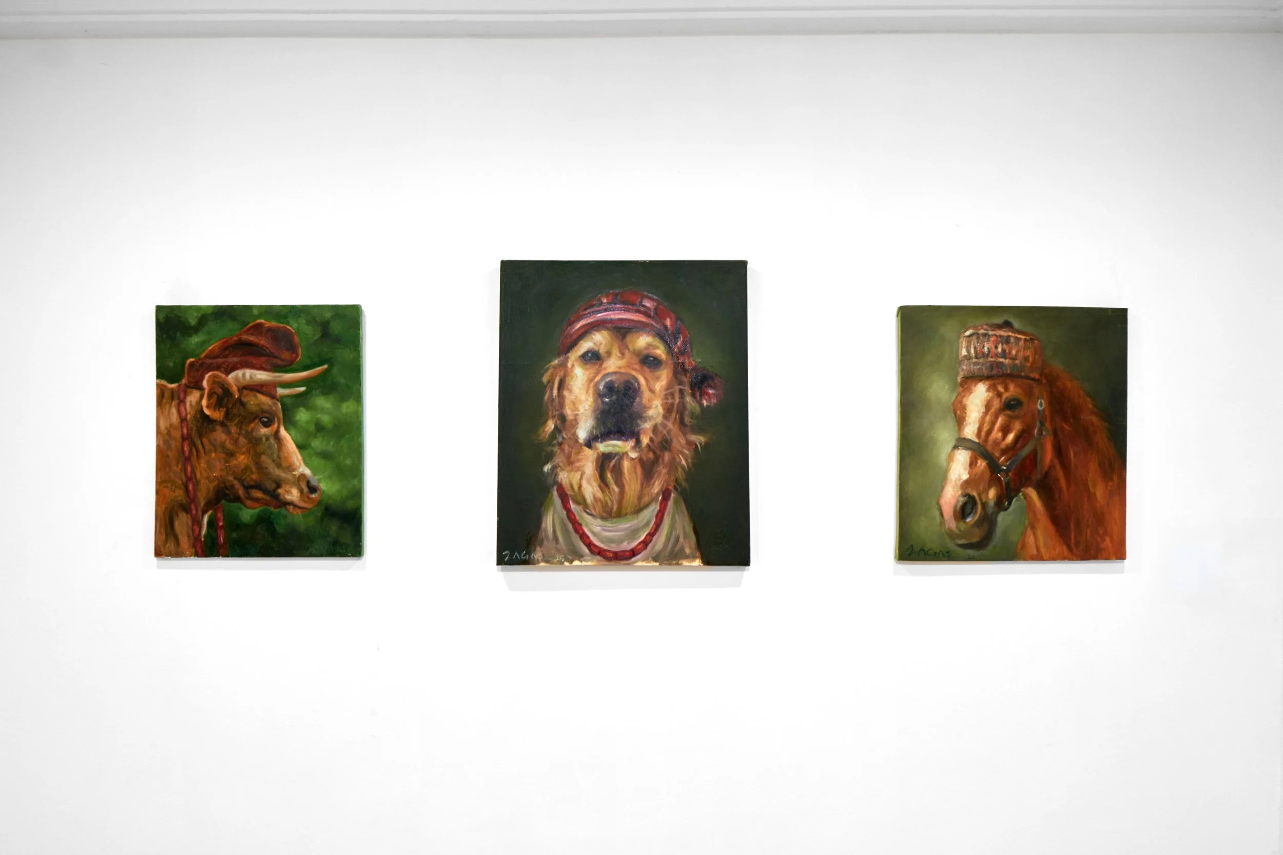 Three animal portrait paintings on a white gallery wall. The left depicts a cow wearing a red hat with a green background, the middle shows a dog with a bandana and red necklace with a dark background, and the right displays a horse with a riding cap and saddle on a green background.