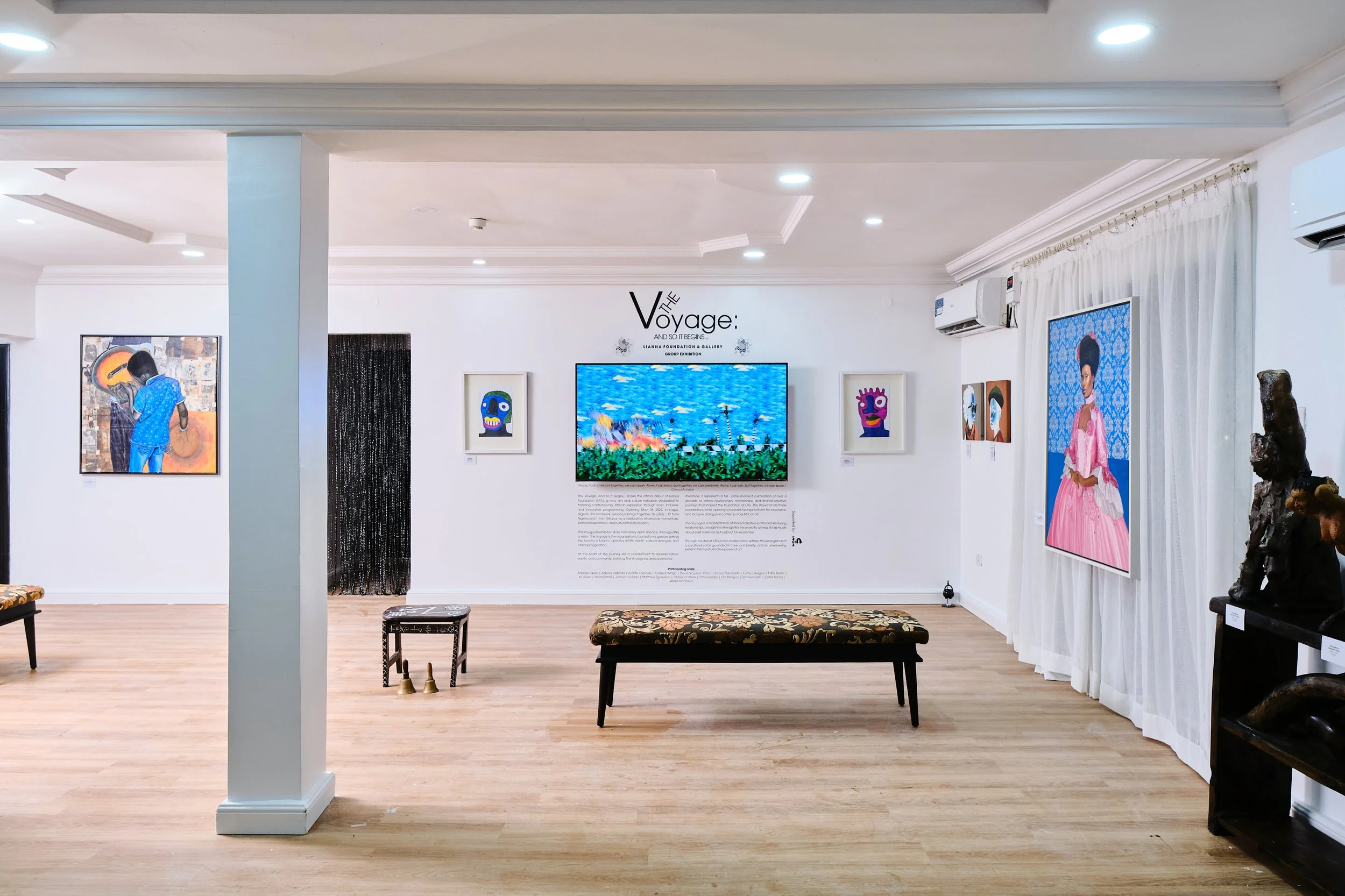 View of an art gallery with various paintings on white walls and a bench in the center. Artwork includes colorful portraits and a landscape painting on a screen, with a text header reading 'The Voyage'.