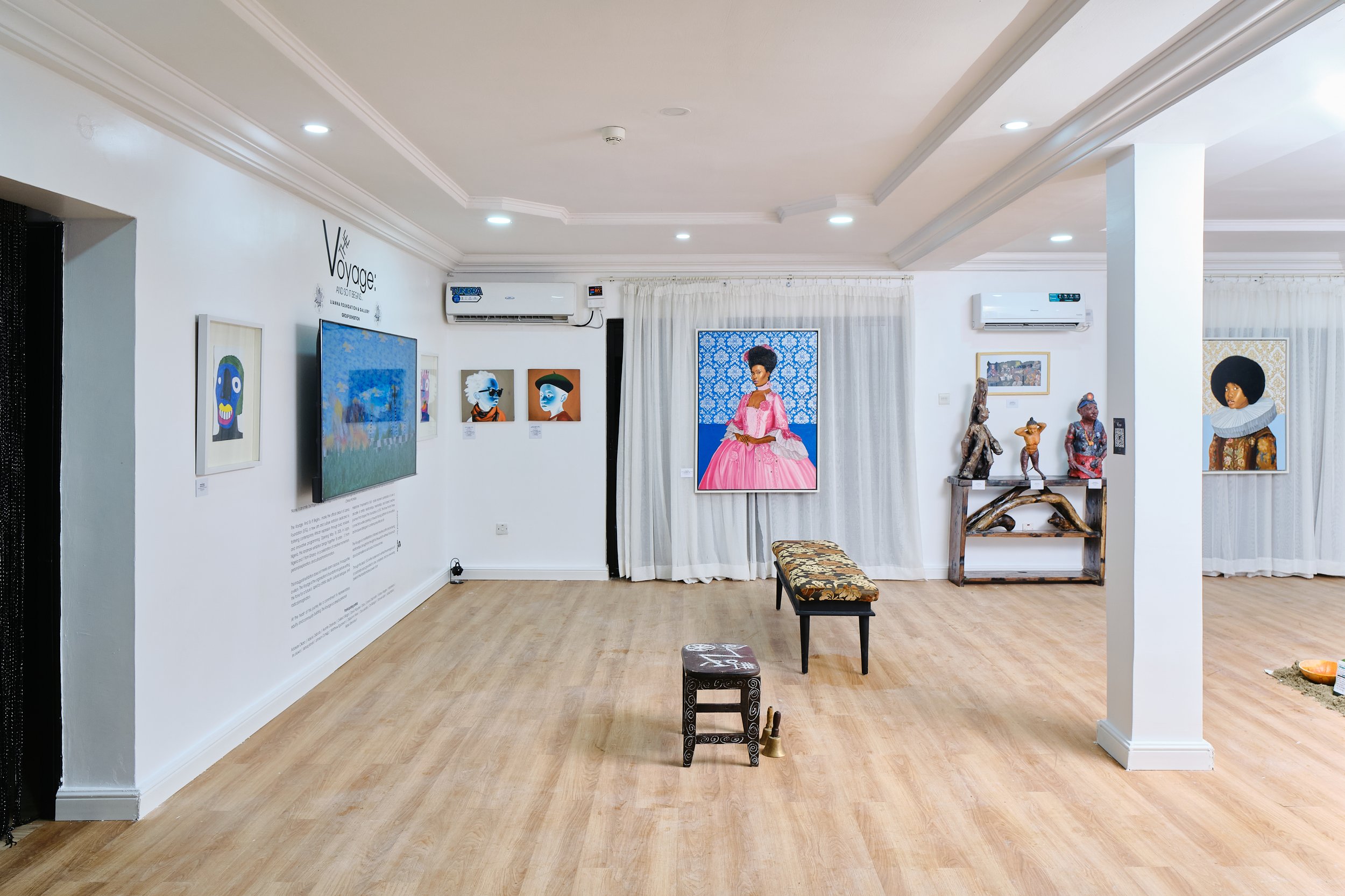 Art gallery interior with paintings and sculptures, benches in center, and wooden flooring.