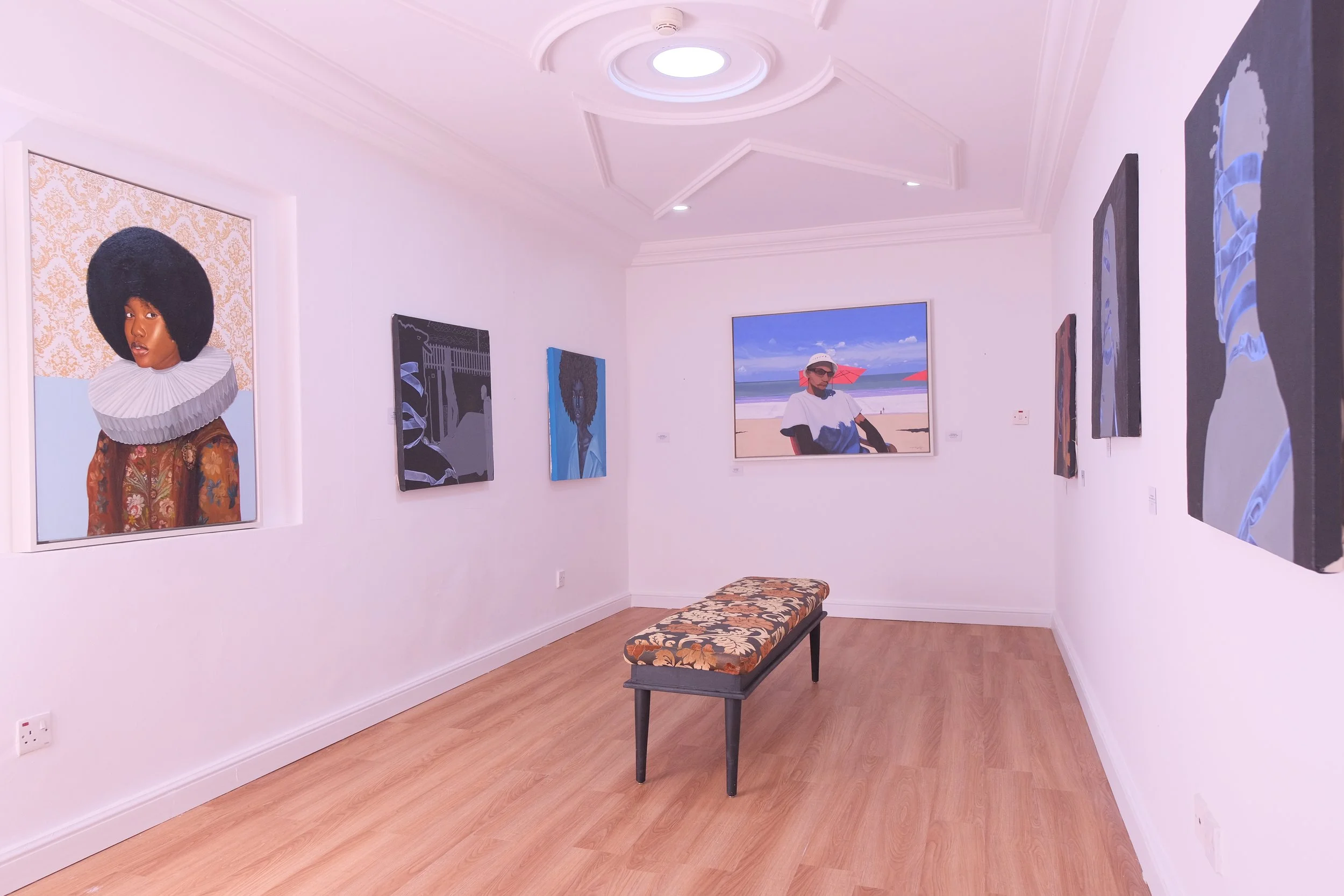Art gallery with paintings on white walls, a bench with floral upholstery in the center, and detailed ceiling moldings.