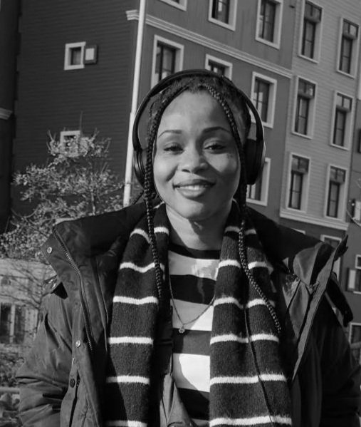 Black woman wearing headphones and a striped scarf outdoors in front of a building.