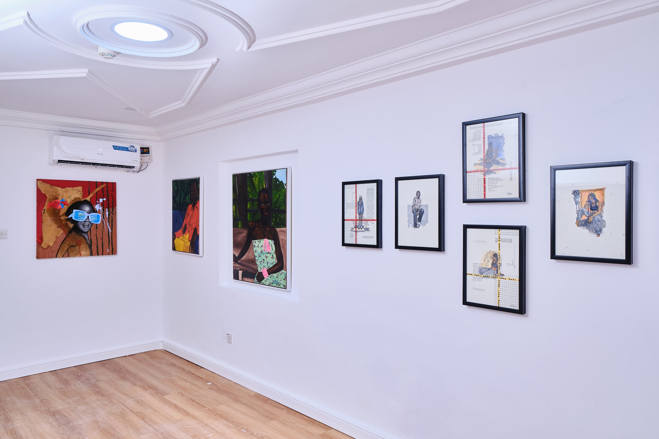 An art gallery with framed artwork on white walls and hardwood flooring.