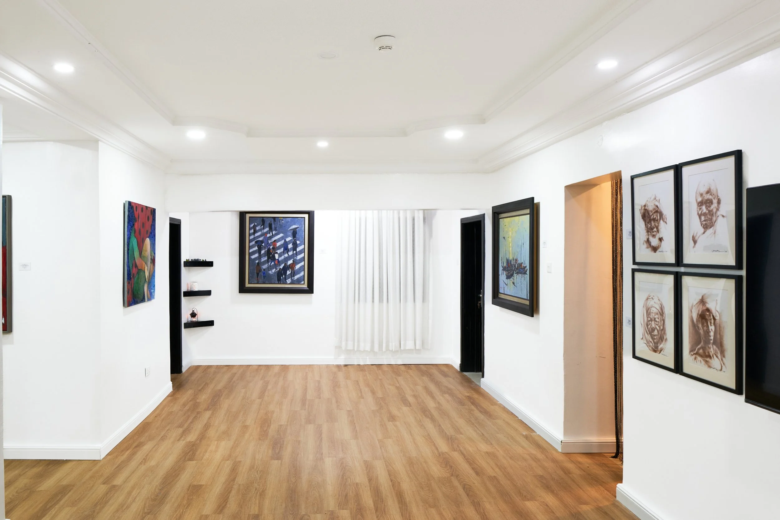 Art gallery with white walls, wooden floor, and various paintings and sketches displayed.
