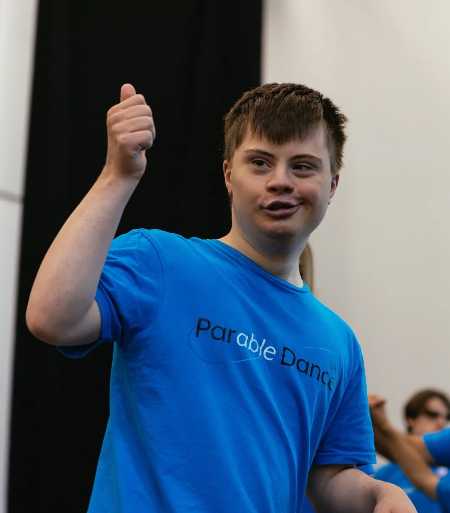 A young boy wearing a blue t-shirt with 'Parable Dance' printed on it, giving a thumbs-up gesture and smiling.