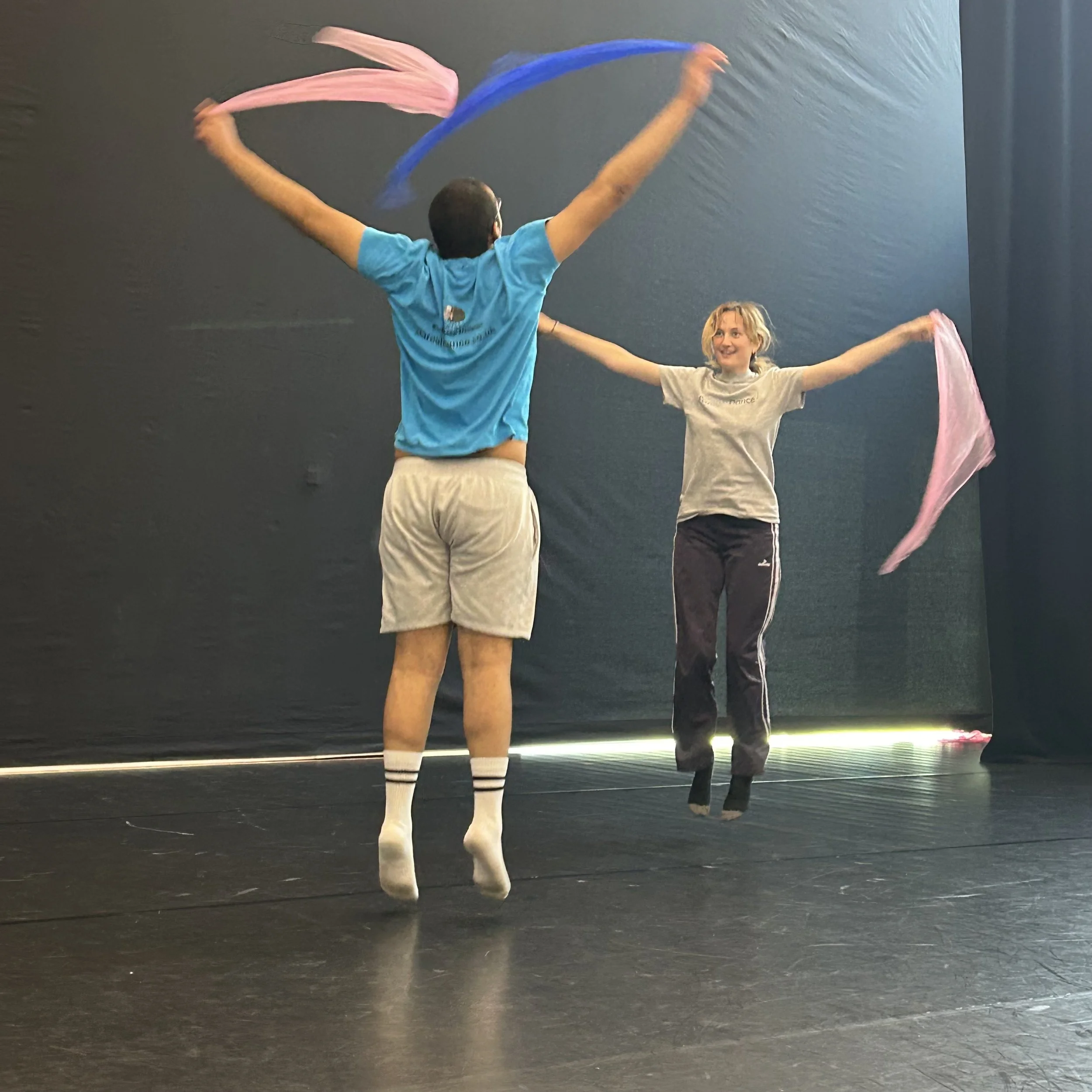 Two people practicing dance with colourful scarves in a black studio.