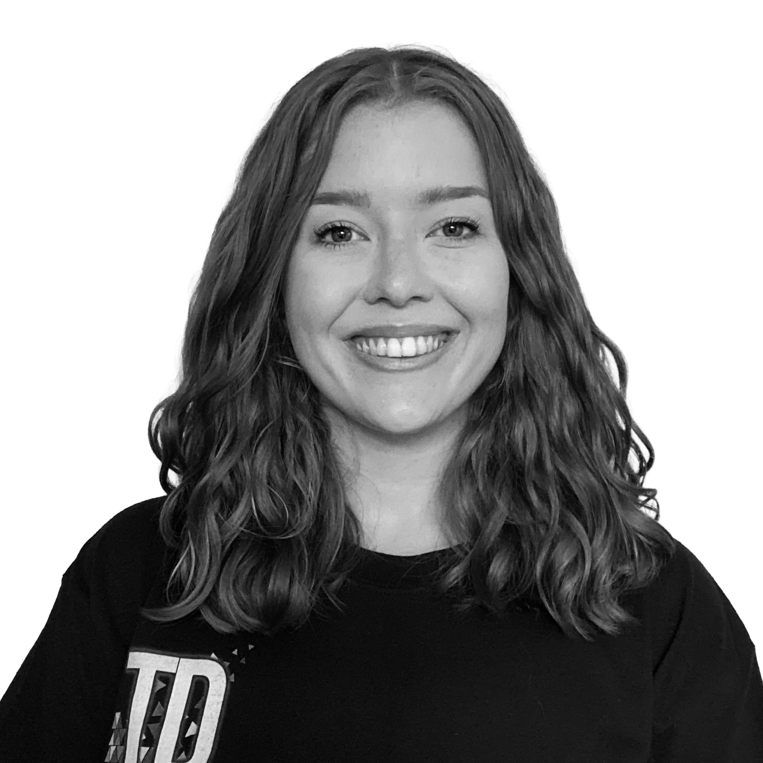 Black and white photograph of a young woman with curly hair smiling, wearing a black shirt with part of a logo visible on the left side.