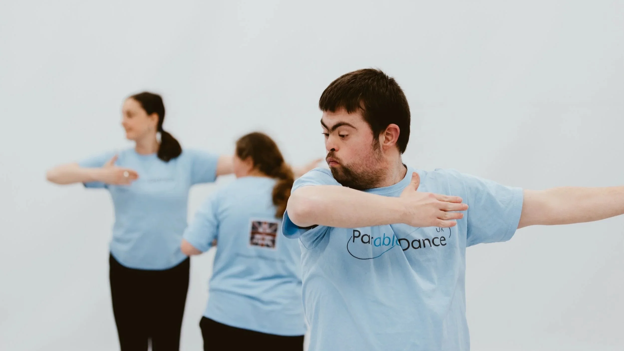 Group of four people practicing dance moves in a studio, all wearing light blue t-shirts.