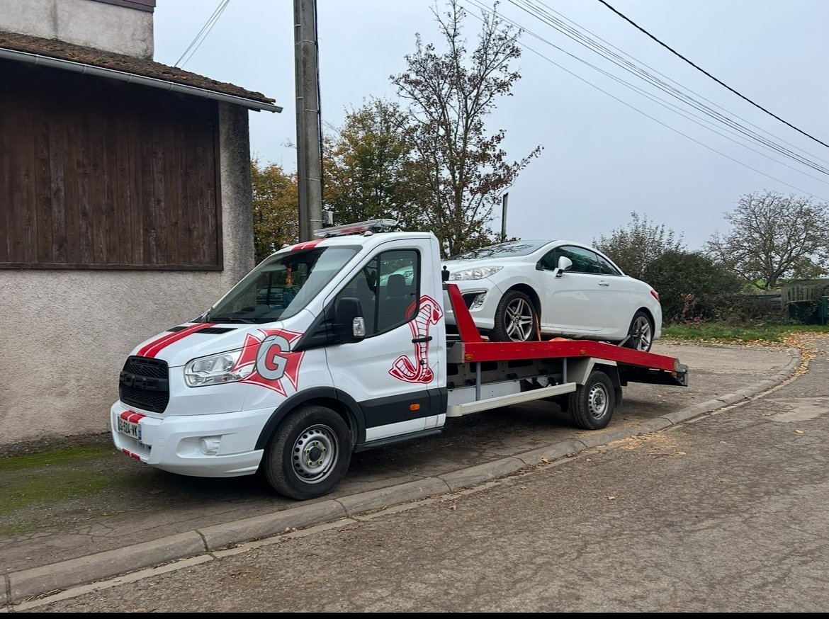 Un camion de remorquage blanc transportant une voiture blanche stationnée sur le bord de la route près d'une maison.