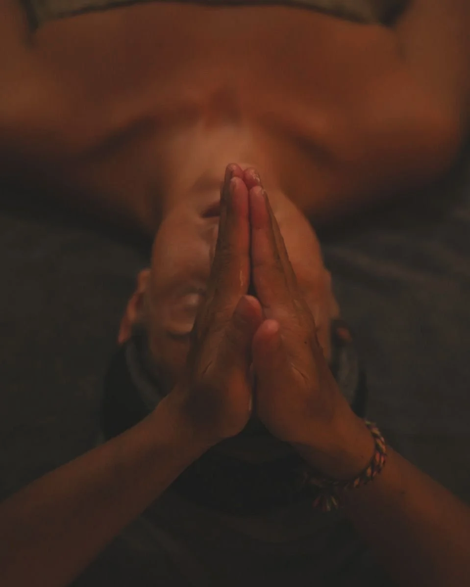 Personne allongée pendant un massage, les mains jointes, dans une ambiance tamisée.