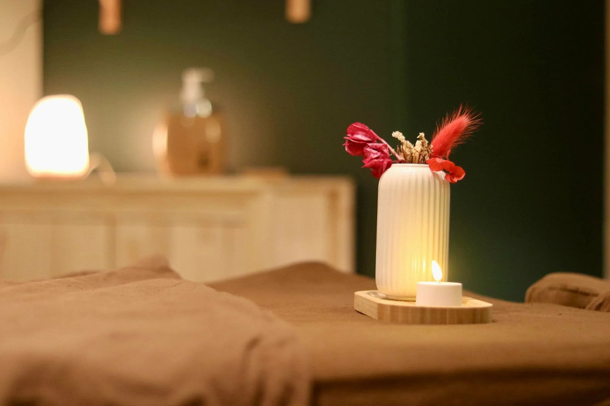 Vase blanche avec fleurs rouges et rouges, à côté d'une petite bougie allumée sur une table en bois