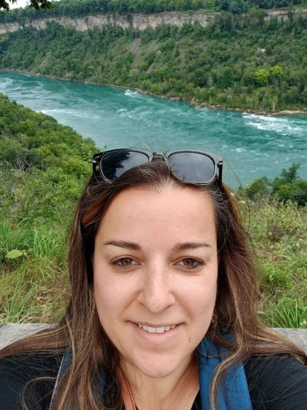 Femme prenant un selfie avec une rivière et une forêt en arrière-plan.