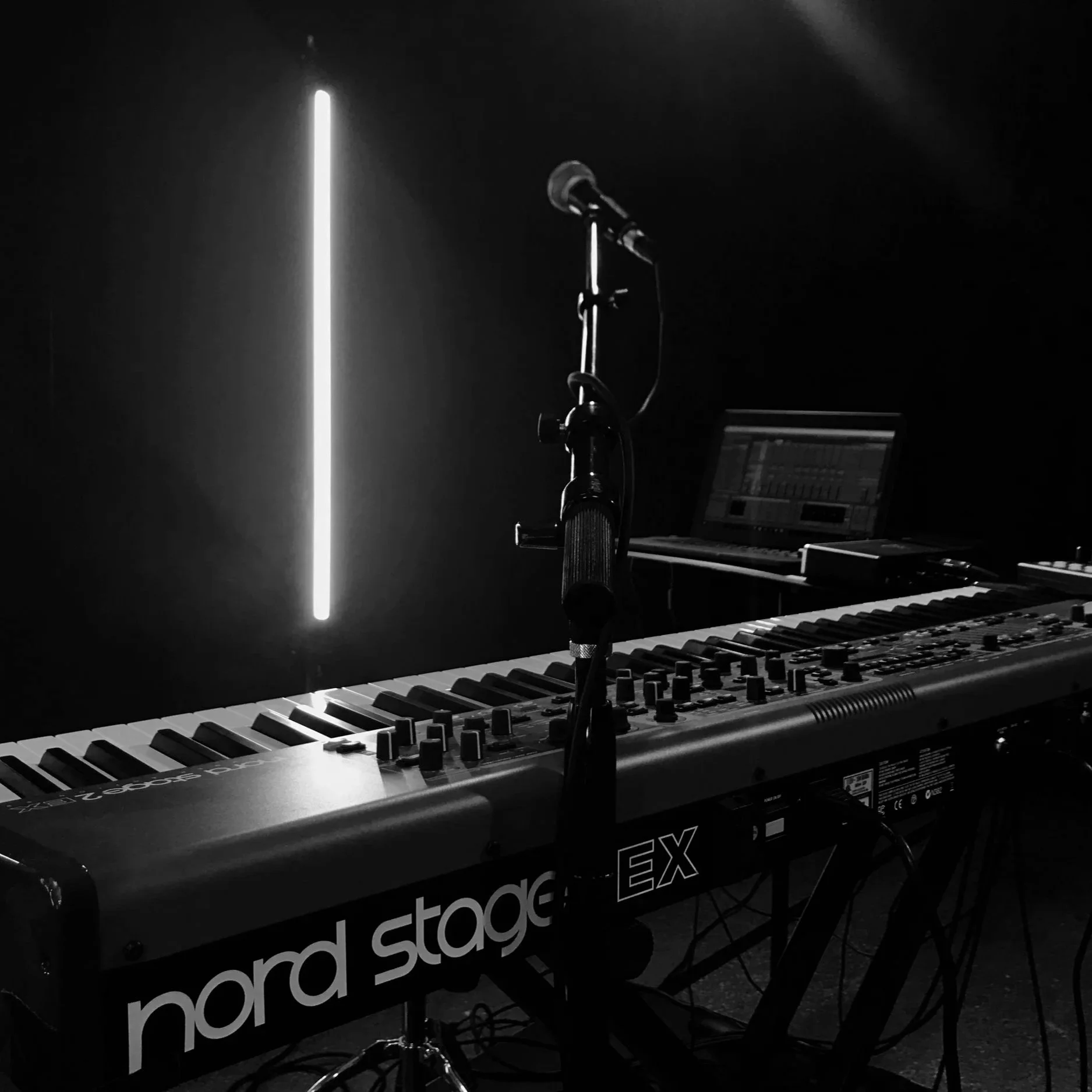 A music studio scene with a keyboard, microphone, and digital audio workstation in a dark setting with a vertical light strip.