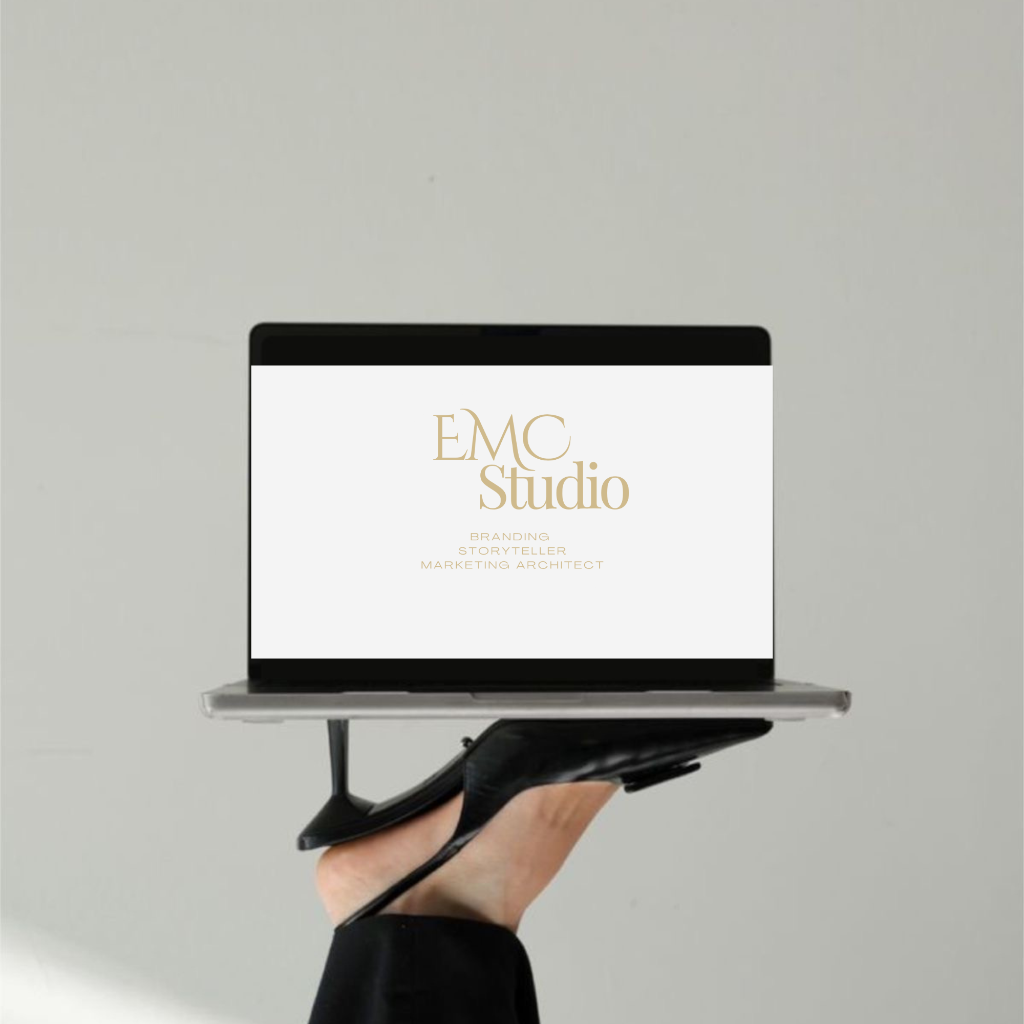Hand holding a laptop with a screen displaying 'EMC Studio' logo and brand Identity.